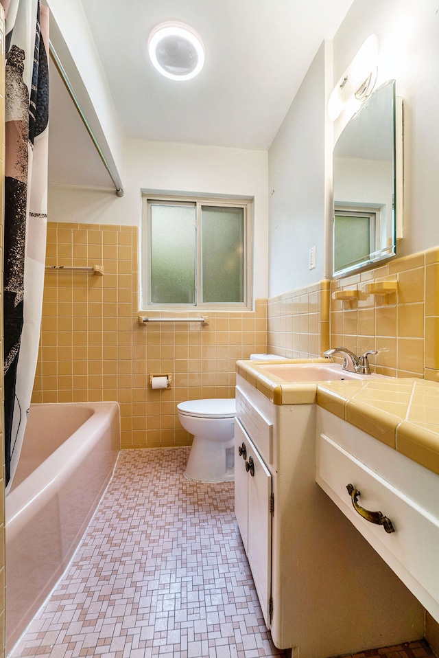 full bath featuring tile walls, toilet, vanity, and wainscoting