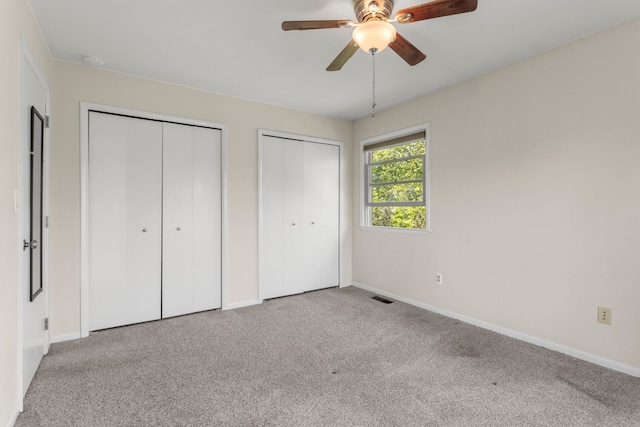 unfurnished bedroom with multiple closets, baseboards, carpet flooring, and a ceiling fan