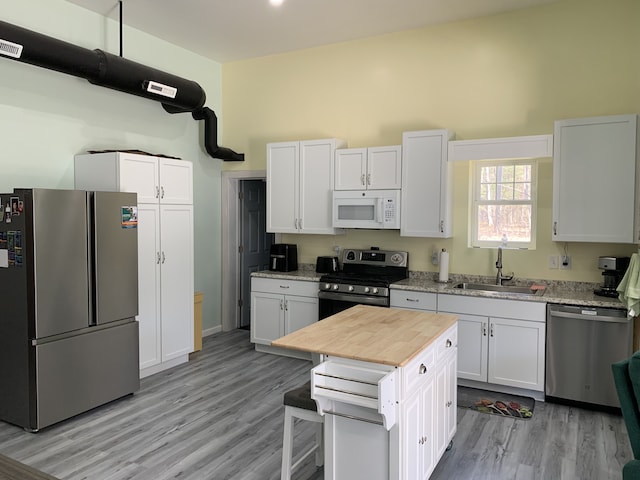 kitchen with appliances with stainless steel finishes, a sink, light wood finished floors, white cabinetry, and a breakfast bar area