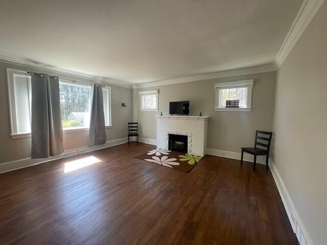 519 Whaley St, Cadillac, MI 49601 - unfurnished living room featuring crown molding, dark wood-type flooring, plenty of natural light, a brick fireplace, and baseboards