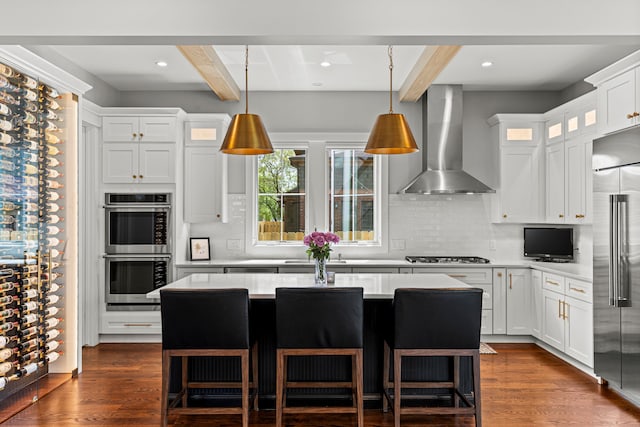 kitchen with wall chimney range hood, stainless steel appliances, beam ceiling, light countertops, and backsplash