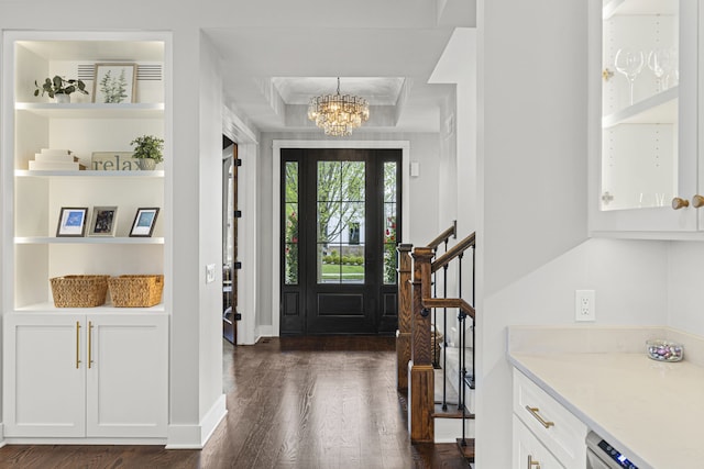 foyer entrance featuring dark wood-type flooring, a chandelier, stairs, baseboards, and a raised ceiling