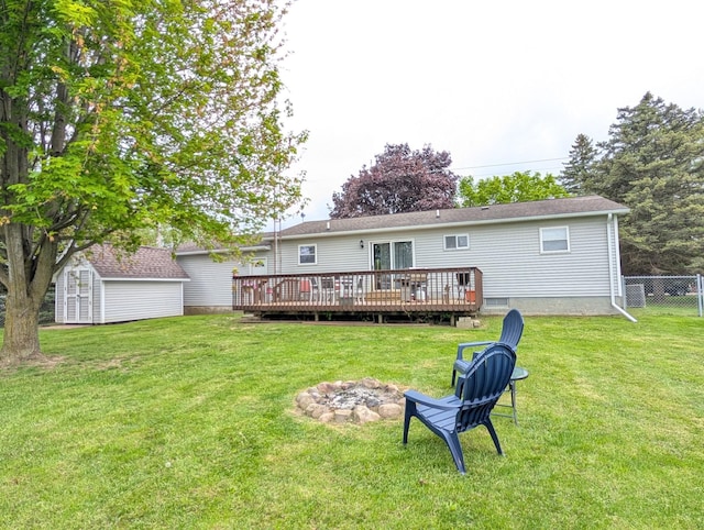 rear view of property featuring a storage shed, a fire pit, a deck, and an outbuilding