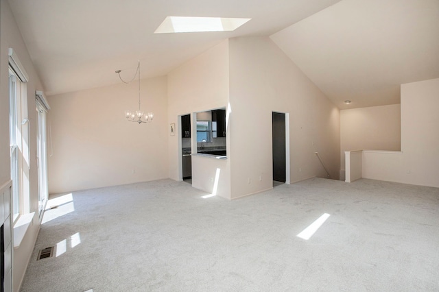unfurnished living room featuring a chandelier, a skylight, light carpet, high vaulted ceiling, and a sink