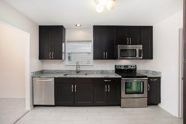 kitchen with stainless steel appliances, a sink, baseboards, and light stone counters