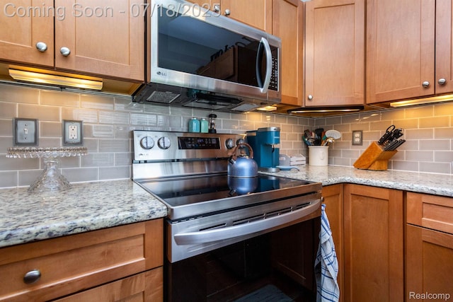 25380 Tara Ln, Flat Rock, MI 48134 - kitchen with appliances with stainless steel finishes, decorative backsplash, brown cabinets, and light stone counters
