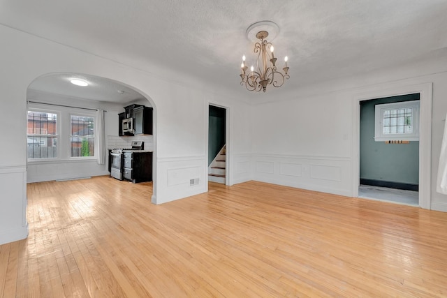 18600 Monica St, Detroit, MI 48221 - unfurnished living room featuring arched walkways, light wood-style floors, a chandelier, stairs, and wainscoting