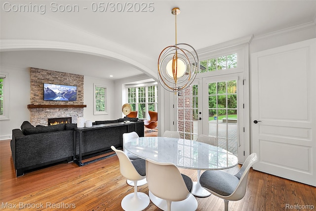 222 Arlington St, Birmingham, MI 48009 - dining space featuring light wood finished floors, crown molding, a stone fireplace, arched walkways, and a chandelier