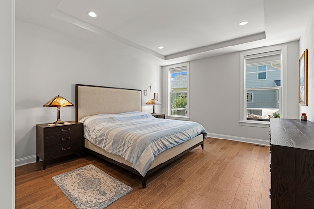 bedroom with a tray ceiling, light wood-type flooring, baseboards, and recessed lighting