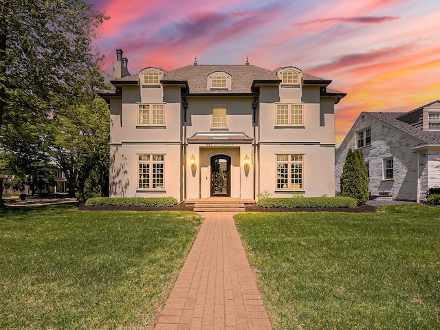 french country inspired facade featuring stucco siding, a yard, and a chimney