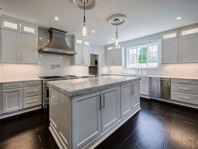 kitchen featuring wall chimney exhaust hood, appliances with stainless steel finishes, a center island, a sink, and tasteful backsplash