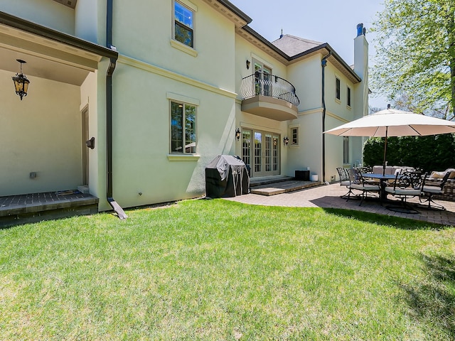 back of house featuring a balcony, french doors, stucco siding, a patio area, and a lawn