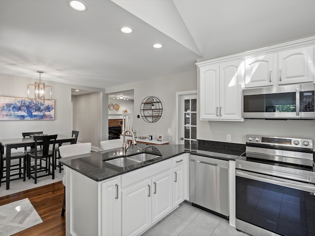 270 S Center St, Northville, MI 48167 - kitchen featuring appliances with stainless steel finishes, a peninsula, a stone fireplace, a sink, and dark stone counters