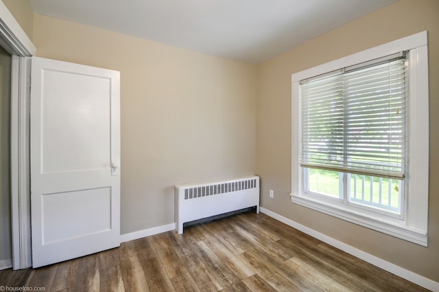 unfurnished bedroom with radiator, wood finished floors, and baseboards