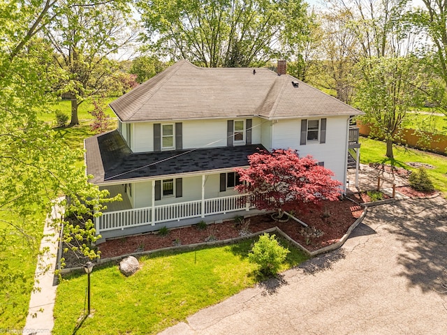 view of front of house featuring a chimney, roof with shingles, and a front lawn