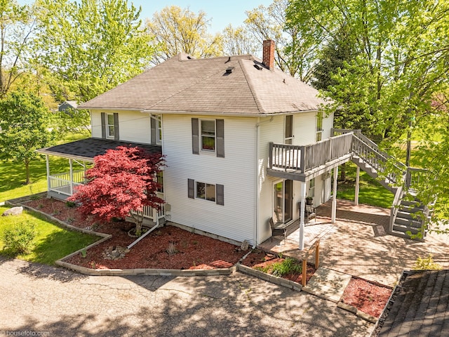 view of side of property featuring a patio area, a chimney, stairs, a shingled roof, and a deck