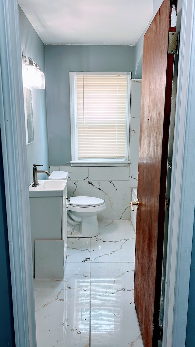 half bathroom with vanity, toilet, and marble finish flooring