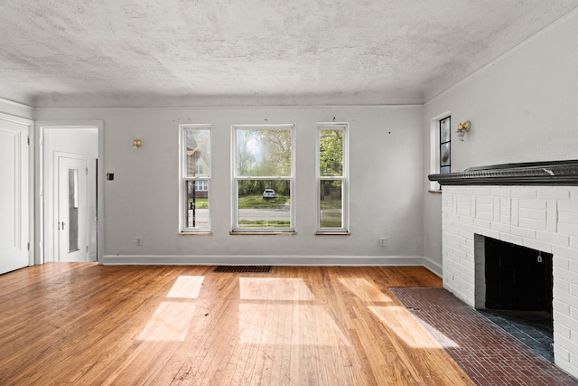 unfurnished living room featuring wood finished floors, a brick fireplace, baseboards, and a textured ceiling