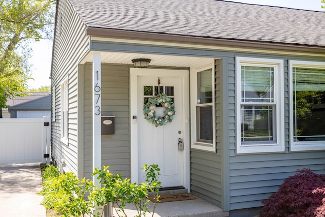 entrance to property with roof with shingles and fence