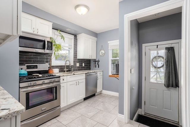 kitchen featuring stainless steel appliances, backsplash, white cabinetry, and baseboards