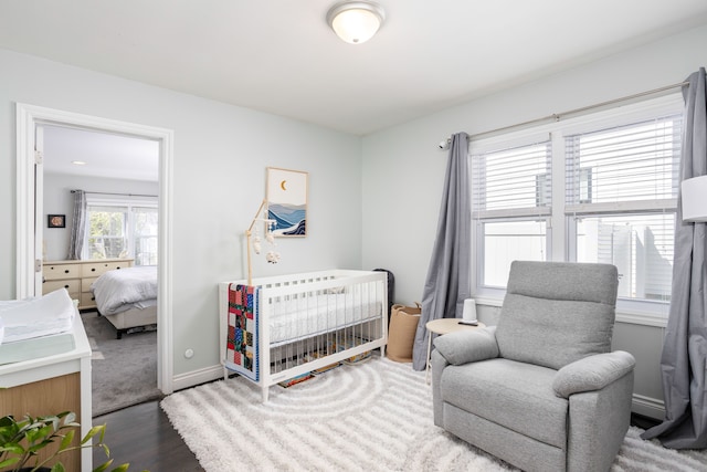bedroom with wood finished floors, a crib, and baseboards