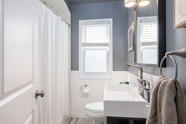 bathroom featuring wainscoting, toilet, healthy amount of natural light, vanity, and a shower with shower curtain