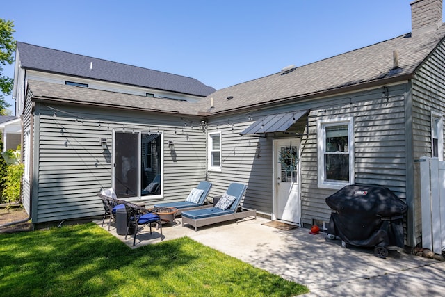 back of house featuring a patio area, a yard, roof with shingles, and a chimney