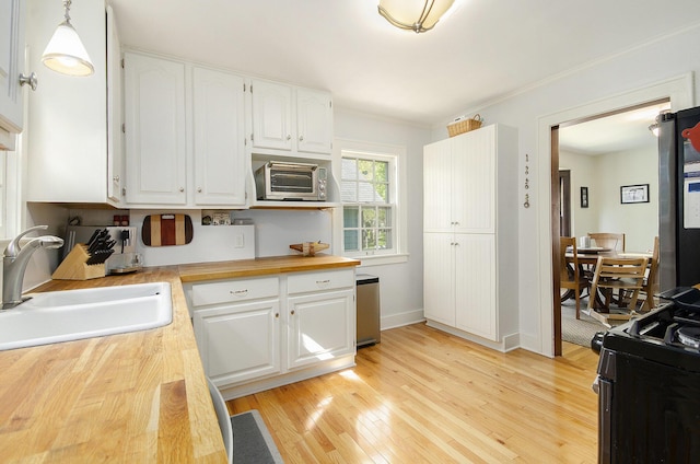 kitchen featuring a sink, wooden counters, range with gas cooktop, white cabinets, and ornamental molding