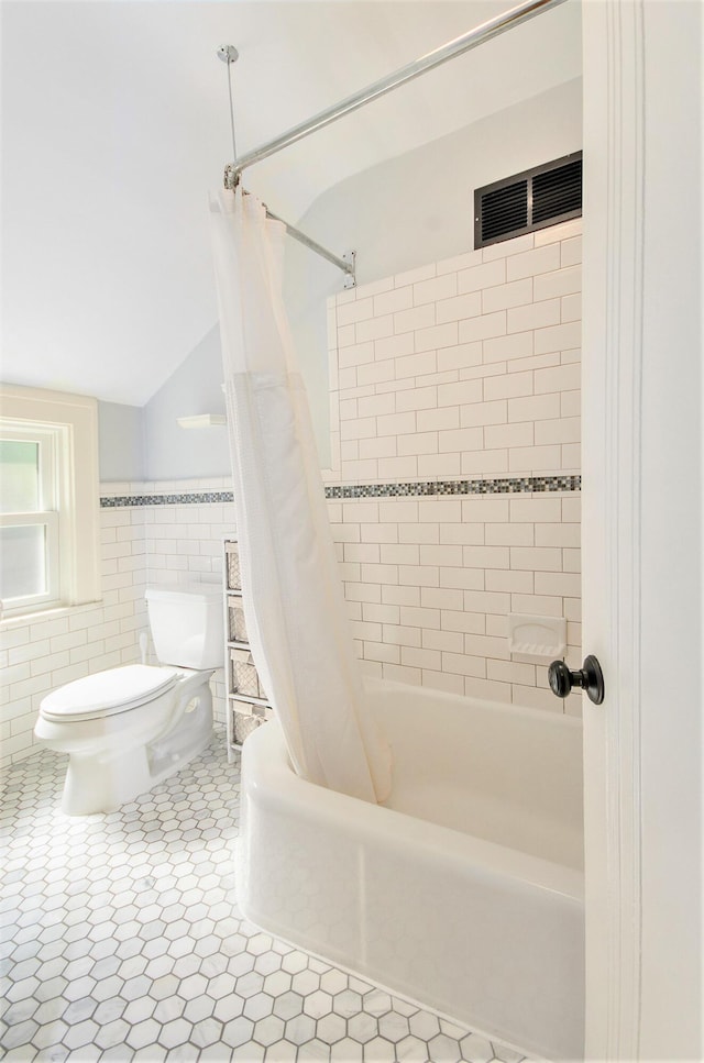 full bath with toilet, tile walls, shower / bath combo with shower curtain, lofted ceiling, and a wainscoted wall