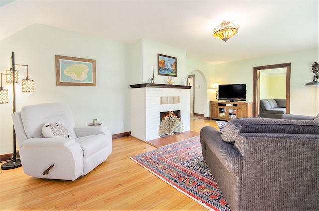 living area with arched walkways, wood finished floors, a fireplace, and baseboards