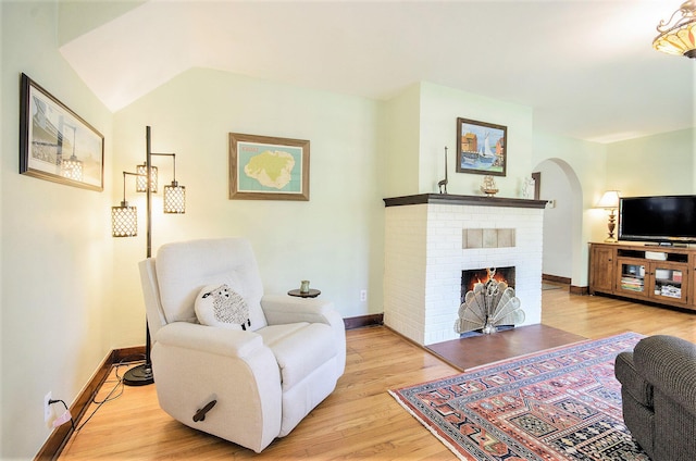 living room with arched walkways, light wood-style floors, baseboards, and a brick fireplace