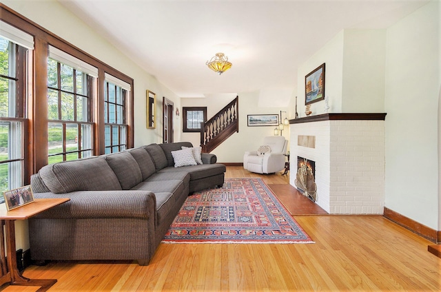 living area with wood finished floors, baseboards, stairs, and a brick fireplace