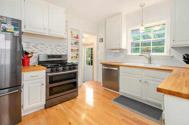 kitchen featuring appliances with stainless steel finishes, a sink, butcher block countertops, white cabinetry, and crown molding