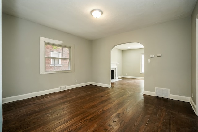 17344 Wisconsin St, Detroit, MI 48221 - empty room with arched walkways, dark wood-type flooring, baseboards, and a fireplace with flush hearth
