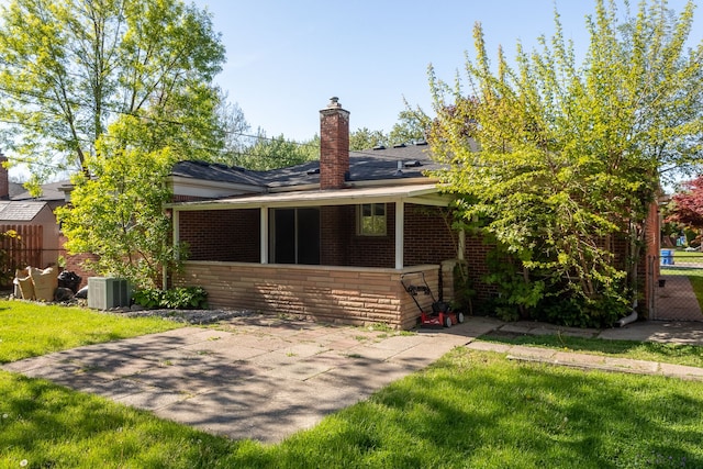 ranch-style home with brick siding, a chimney, a patio, cooling unit, and a sunroom