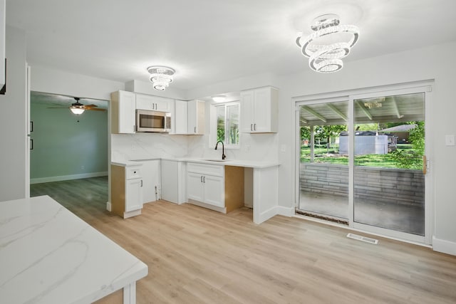 kitchen with stainless steel microwave, light wood-style flooring, a chandelier, light stone countertops, and white cabinets