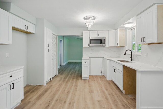 kitchen with stainless steel microwave, a sink, light wood-type flooring, tasteful backsplash, and white cabinets
