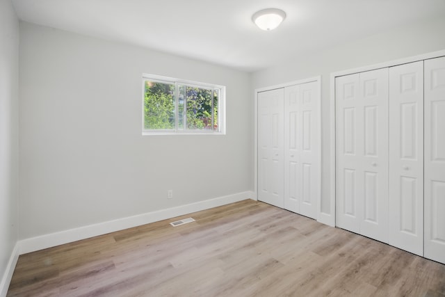 unfurnished bedroom featuring two closets, light wood-style flooring, and baseboards