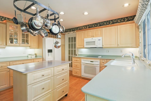 kitchen featuring white appliances, a sink, light brown cabinets, a center island, and light wood-style flooring