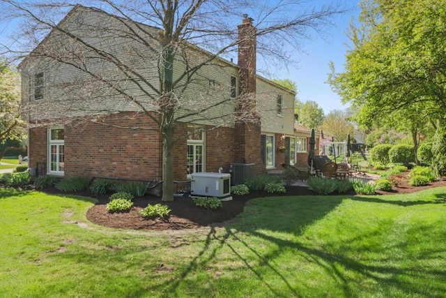 view of side of property with a patio, a lawn, brick siding, and a chimney