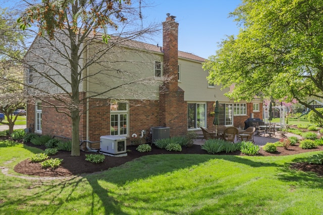rear view of property featuring a patio area, a lawn, central AC unit, a chimney, and brick siding