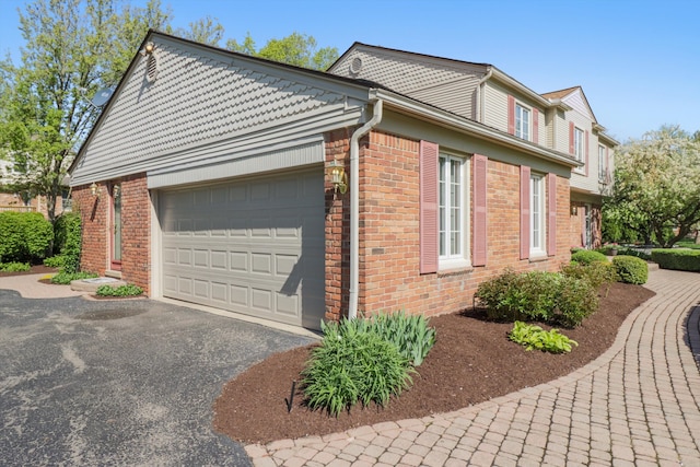 view of property exterior with brick siding, a garage, and driveway