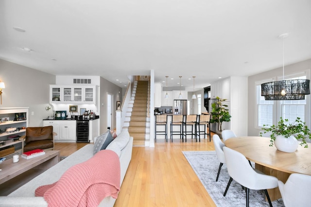 dining space featuring bar area, light wood-type flooring, beverage cooler, and stairway