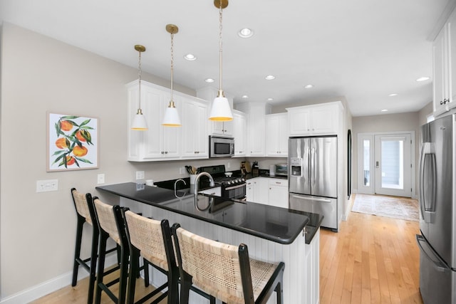 kitchen with stainless steel appliances, a peninsula, dark countertops, white cabinetry, and light wood-style floors