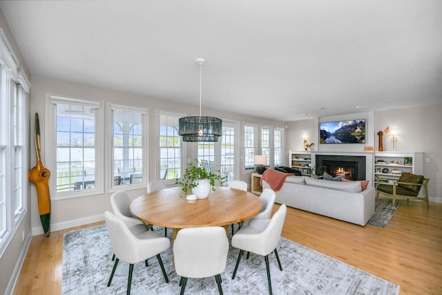 dining room with light wood finished floors, baseboards, a glass covered fireplace, and a chandelier