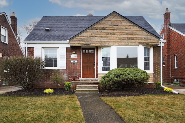 view of front facade with a front lawn, roof with shingles, and brick siding