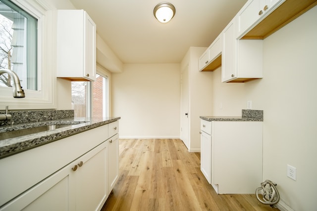 kitchen with a sink, dark stone counters, light wood-style flooring, and white cabinets