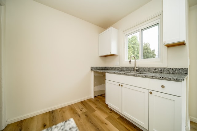 kitchen featuring a sink, light wood finished floors, baseboards, light stone countertops, and white cabinets