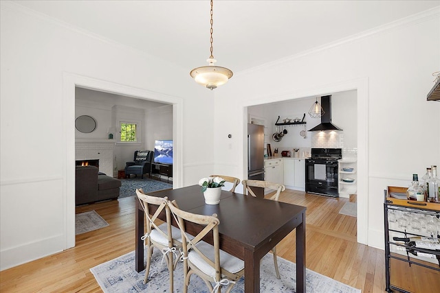 dining area with light wood-type flooring, crown molding, and a lit fireplace