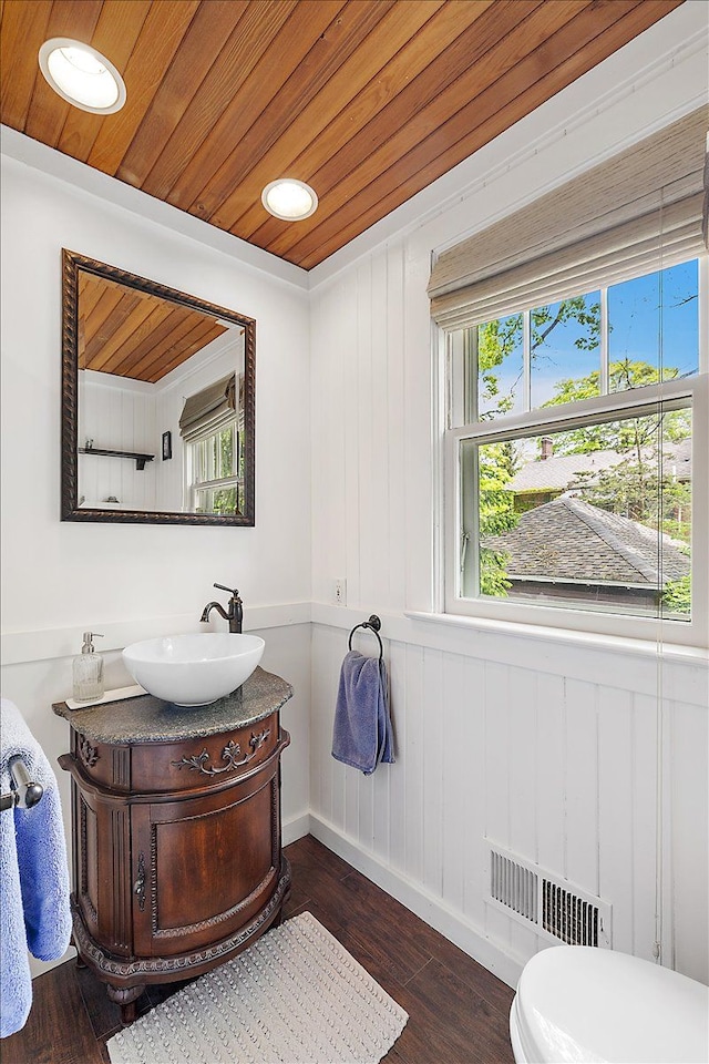 half bath featuring wooden ceiling, vanity, wood finished floors, baseboards, and toilet